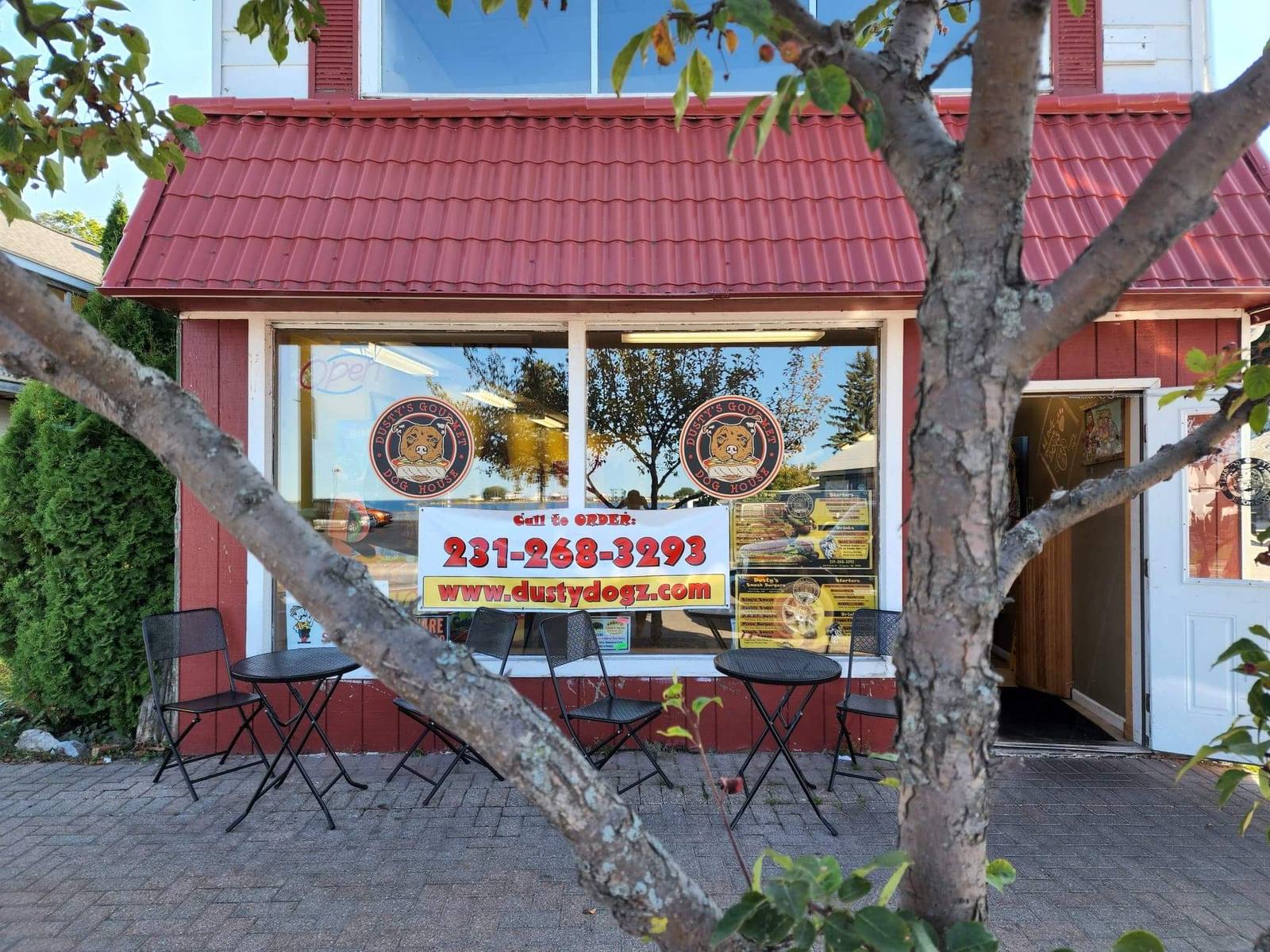 Dusty's Gourmet Dog House storefront: red building with sidewalk tables and the bay reflected in the window